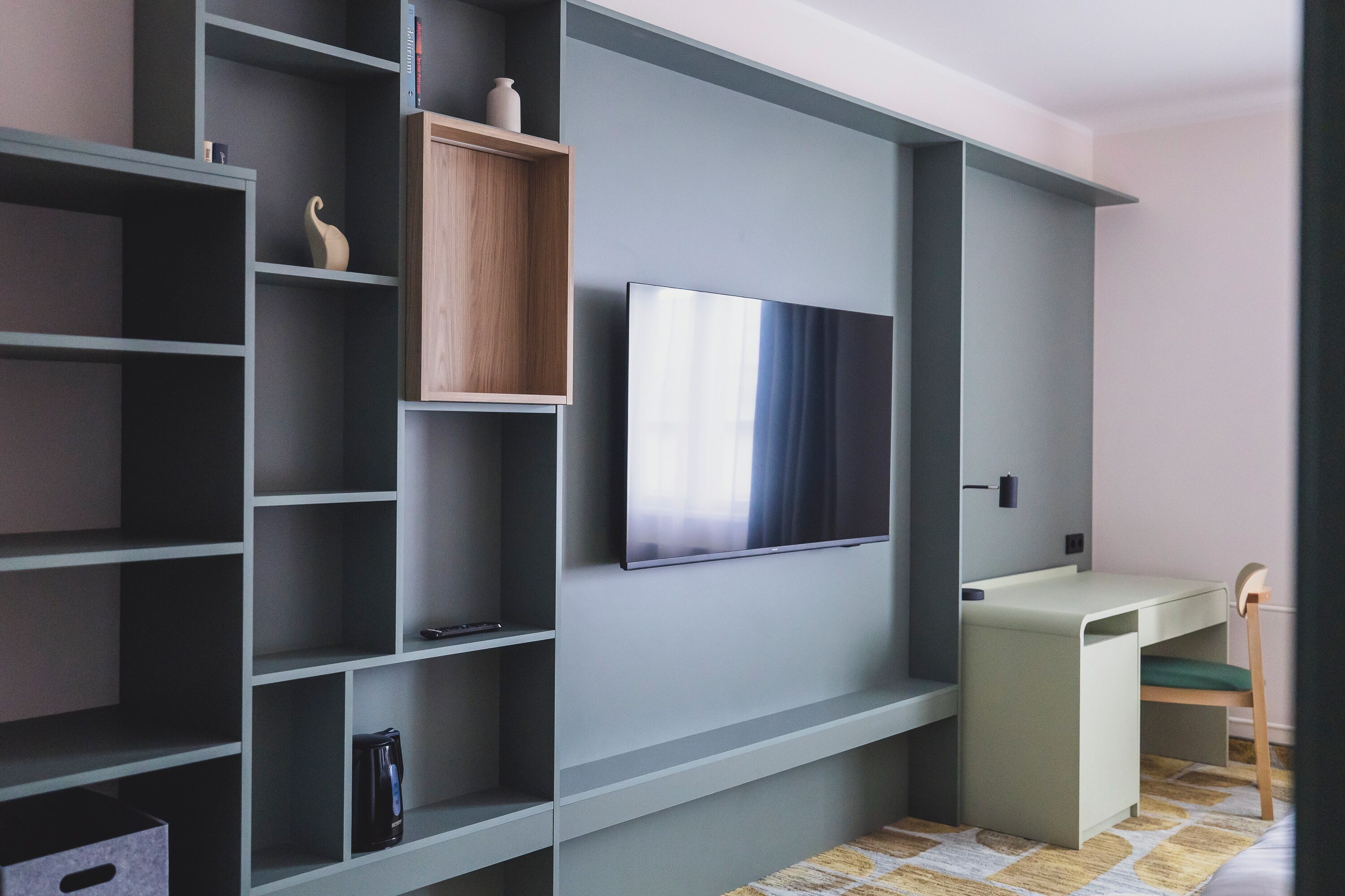 A modern room with built-in shelving, a flat-screen TV, and a desk with a chair.