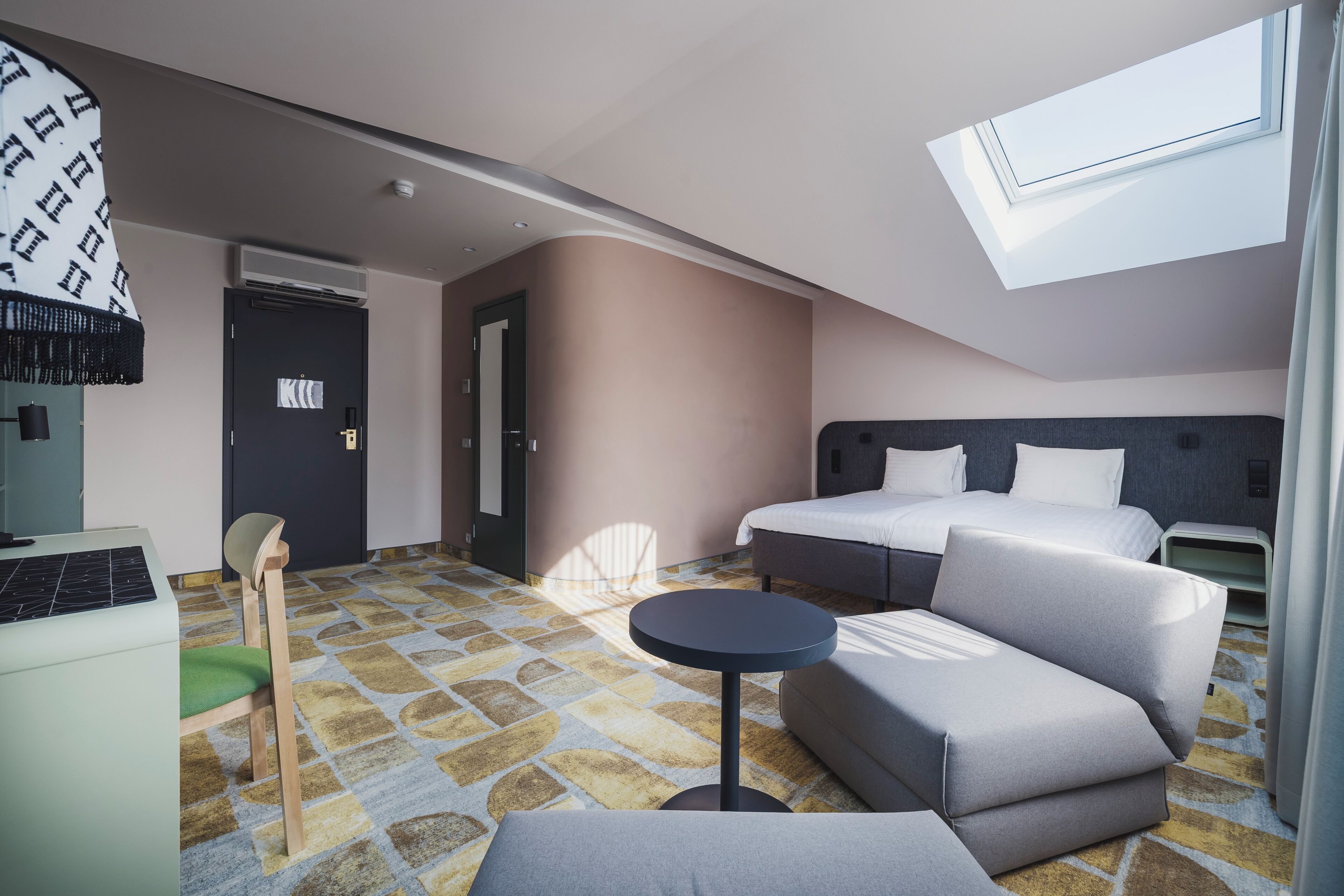 A hotel room with a bed, a sofa, a small table, a desk with a computer, and a window with a view.