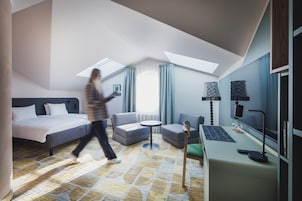 Una habitación de hotel moderna con cama, sofá, escritorio y un ventanal grande.