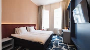 Ein Hotelzimmer mit Bett, Nachttischen, Schreibtisch, Stuhl, Fernseher und einem Fenster mit Vorhängen.