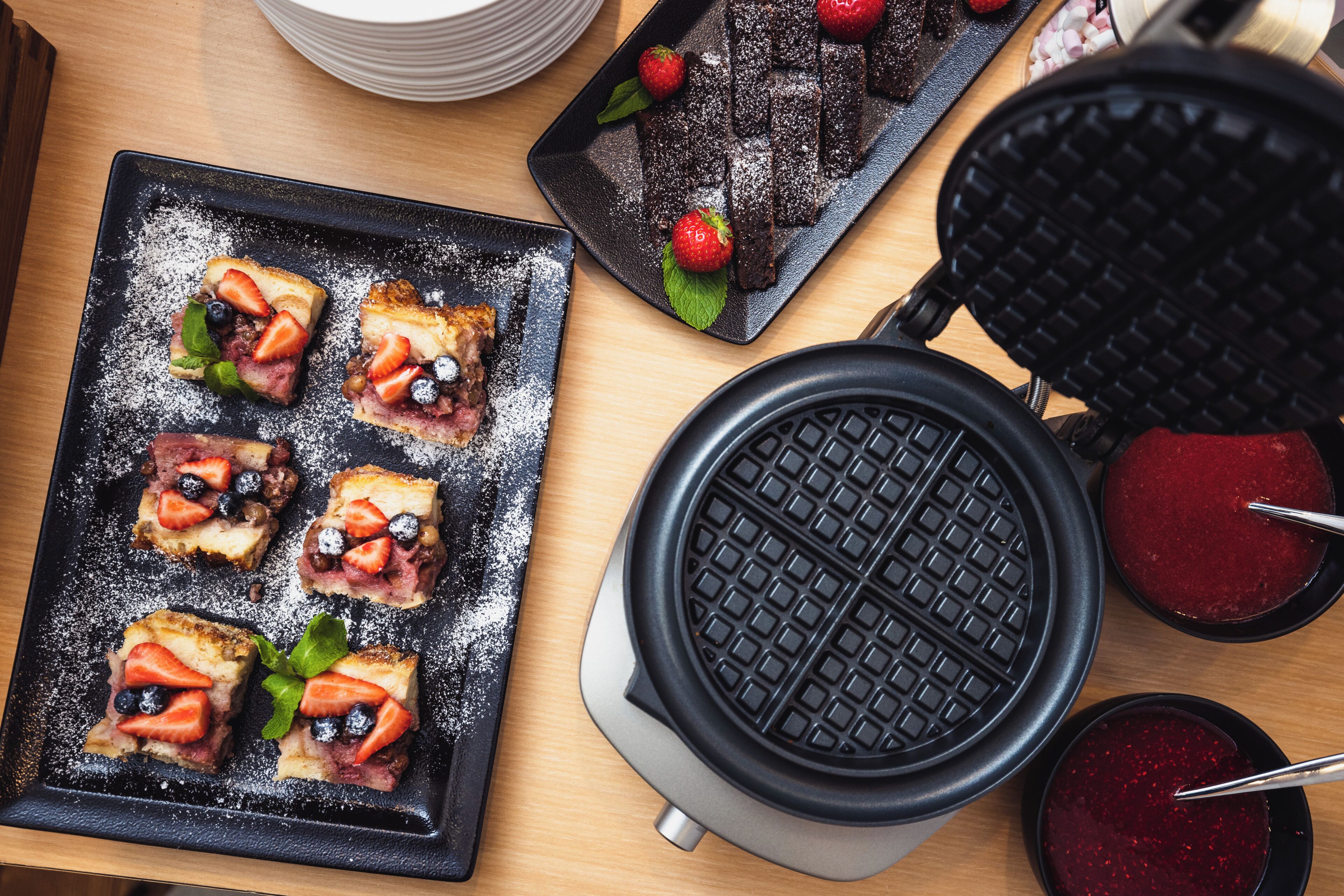 A waffle iron and a plate with waffles topped with strawberries and blueberries.