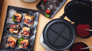A waffle iron and a plate with waffles topped with strawberries and blueberries.