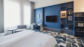 Hotellihuone, jossa on sänky, työpöytä, tuoli, televisio ja kirjahylly.