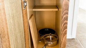 A wooden cabinet with a shelf and a drawer, containing a frying pan, a pot, and a spatula.