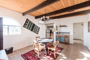 A dining area with a round table, chairs, and a red rug. There is a kitchen in the background with a countertop and cabinets.