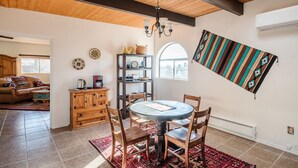 A dining area with a round table, wooden chairs, a chandelier, and a patterned rug.