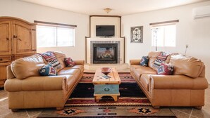 A living room with two leather sofas, a wooden coffee table, a fireplace, and a television above it.