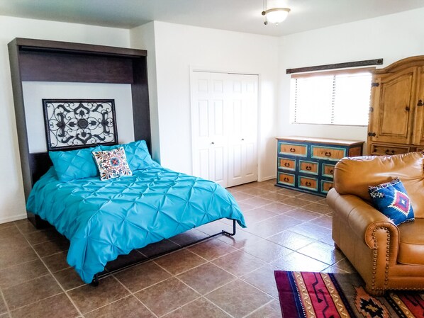 Un dormitorio con cama, cómoda, sofá de cuero marrón y alfombra estampada.