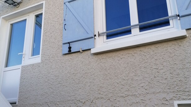 Une façade d’immeuble avec trois fenêtres, chacune dotée d’un cadre blanc et de volets bleus.