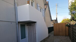 Un immeuble résidentiel à l’extérieur blanc, doté d’une entrée sécurisée par un portail, d’un petit patio avec une table en bois et d’une clôture en bois.