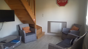 Un salon avec des meubles en osier, un téléviseur, un panneau de signalisation indiquant un arrêt obligatoire et un escalier.