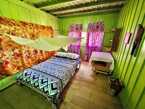 A small, green-painted room with a single bed, a small table, and a mirror on the wall. - Amazonas Maloca Barü, Hostel Tikuna Macedonia  (Leticia)