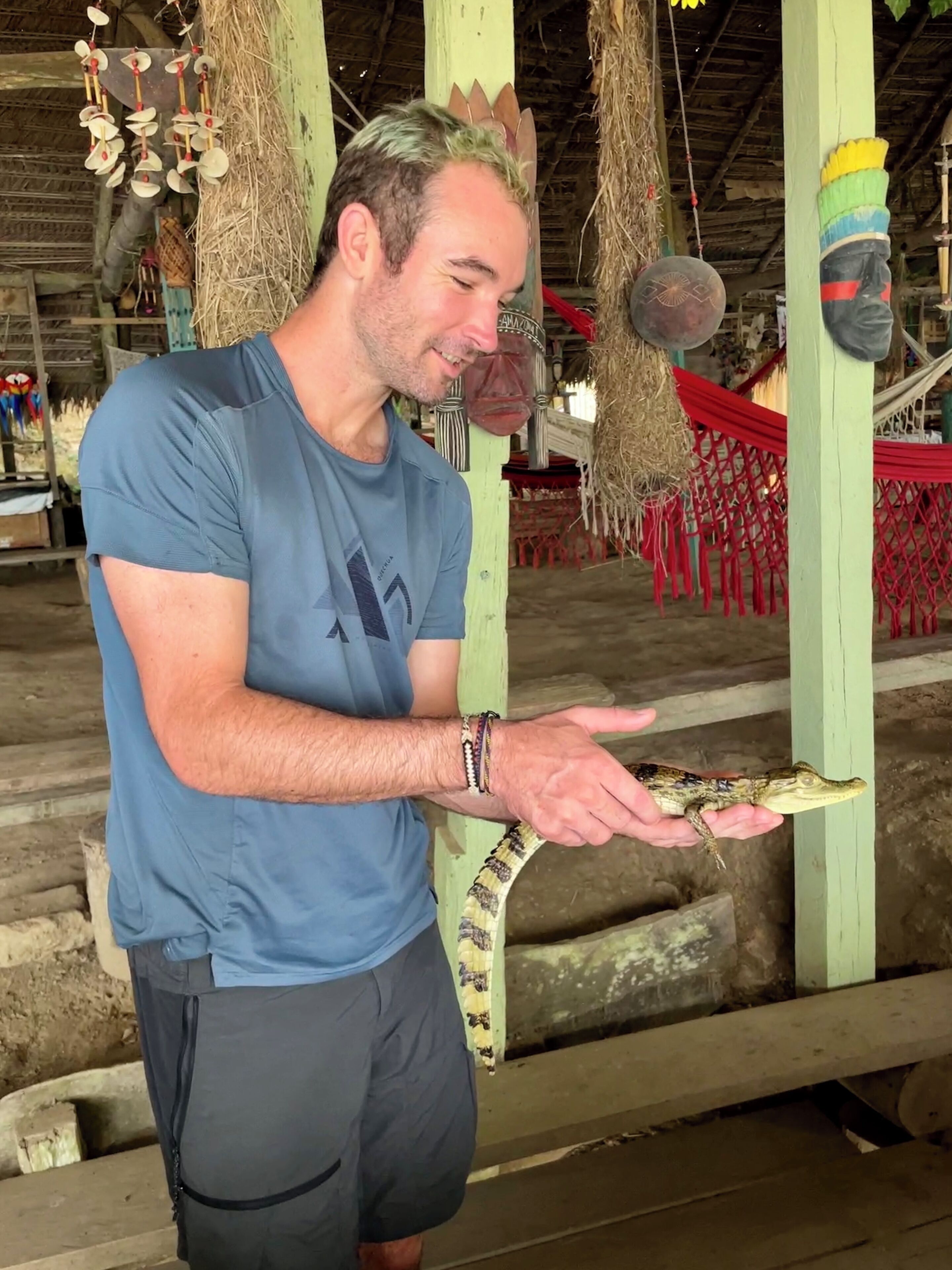A person holding a snake in a rustic setting with wooden structures and hanging decorations.