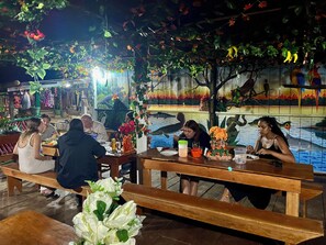 A restaurant with wooden tables and benches, decorated with flowers and hanging decorations. - Amazonas Maloca Barü, Hostel Tikuna Macedonia  (Leticia)