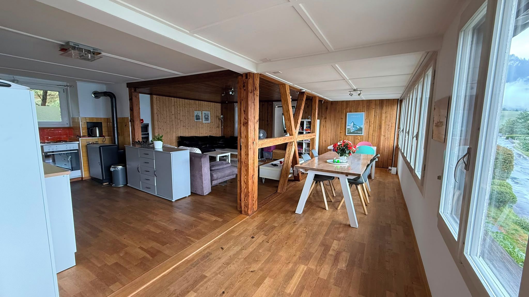 A spacious living area with a wooden floor, a dining table with chairs, and a kitchen area with modern appliances.