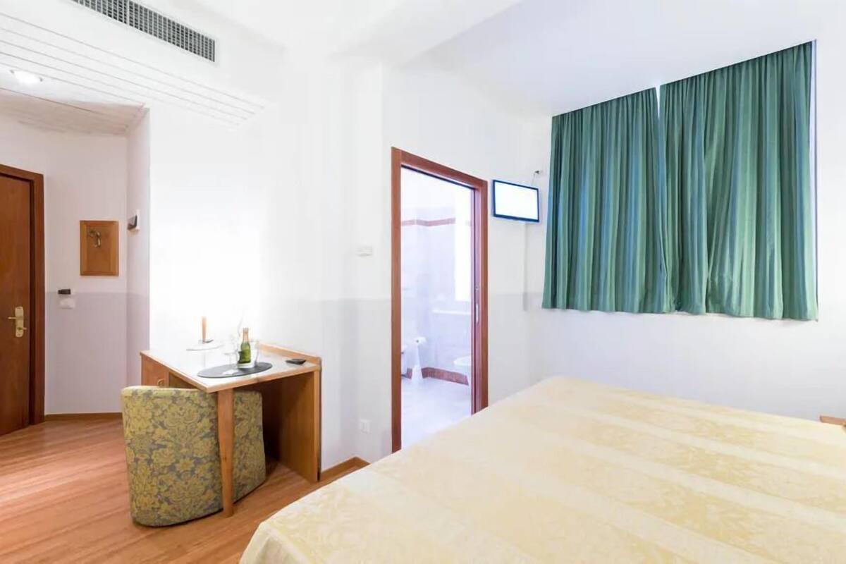 Une chambre à coucher avec un lit, un bureau, une chaise et une fenêtre avec des rideaux.