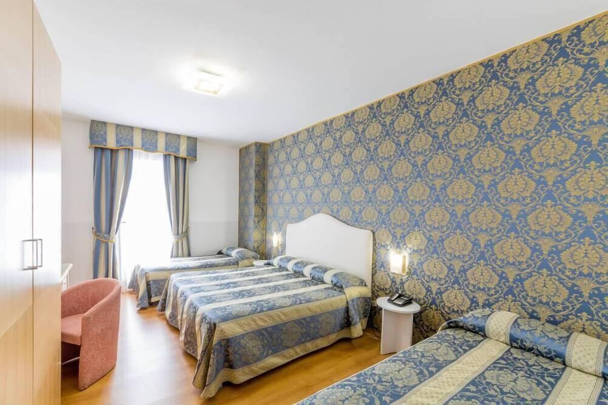 Une chambre d’hôtel avec trois lits, une chaise et une petite table avec une lampe.