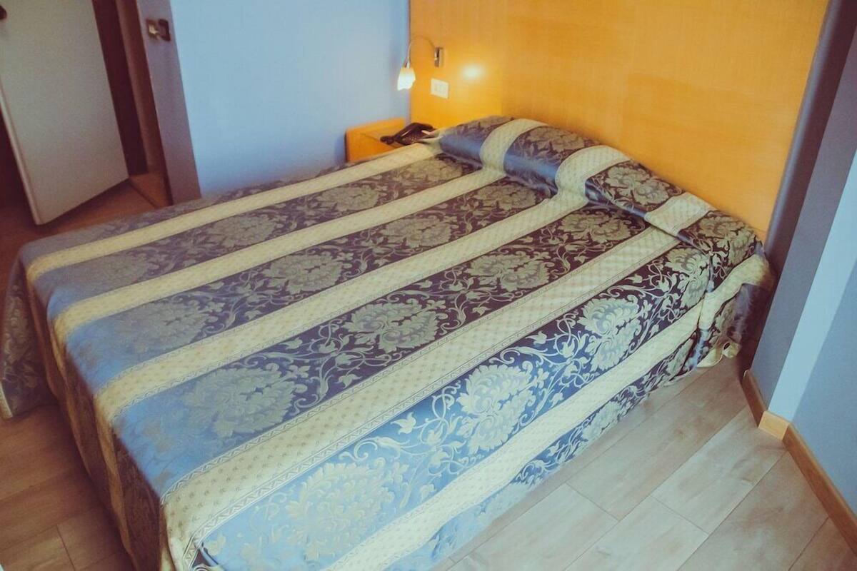 Un lit simple avec une couvre-lit à motifs, une lampe de chevet et une table de chevet avec un téléphone.