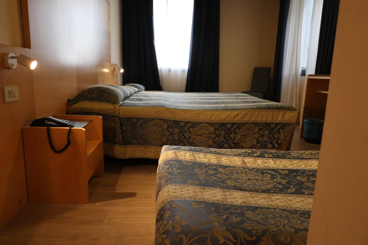 Une chambre d’hôtel avec deux lits, une commode en bois et une table de chevet avec une lampe.