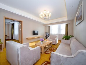 A modern hotel room with a sofa, armchair, a small table with a vase, a TV, and a chandelier. - Vienna International Hotel (Zhongxiang)