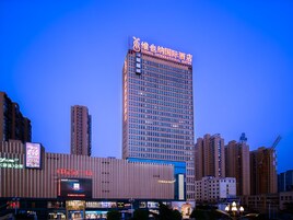 Un hotel de gran altura con un letrero llamativo en la parte superior, rodeado de otros edificios y una zona comercial con letreros iluminados.
