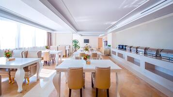 Un comedor de hotel moderno con varias mesas y sillas, una barra de buffet y un amplio ventanal que proporciona luz natural.