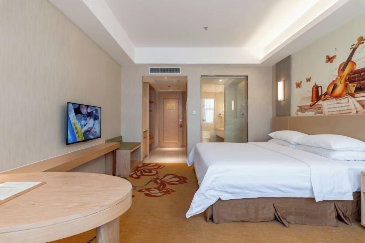A hotel room with a bed, a TV, a desk, and a carpeted floor.