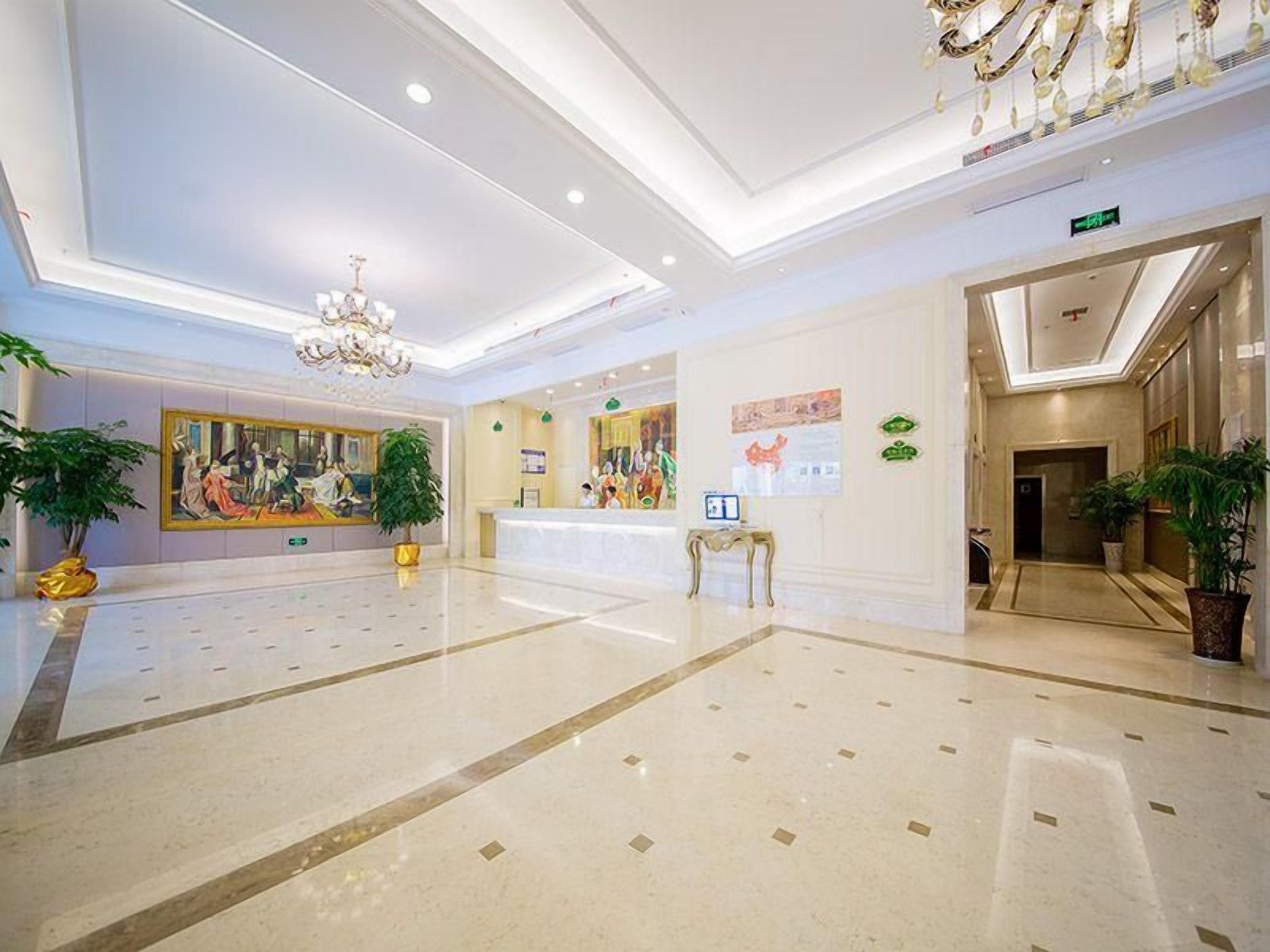 Un hall de hotel con una recepción, una araña y obras de arte en las paredes.