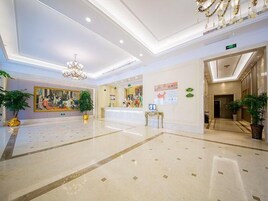 Un hall de hotel con una recepción, una araña y obras de arte en las paredes.