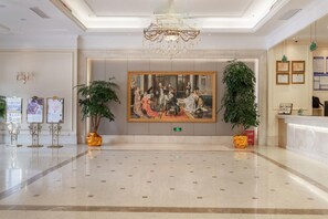 A lobby with a large classical painting, two potted plants, a reception desk, and a chandelier. - Vienna International Hotel (Zhongxiang)