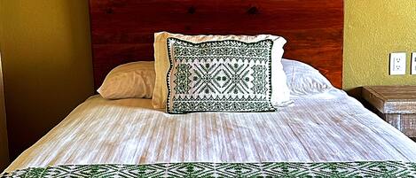 Una cama con cabecera de madera, almohada estampada y manta verde y blanca.