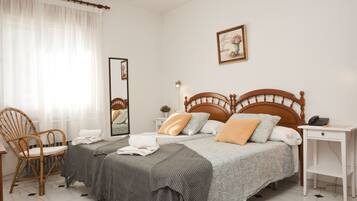 A hotel room with a double bed, a bedside table, a chair, a mirror, and a picture on the wall.