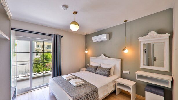 Ein modernes Schlafzimmer mit einem großen Bett, einem Nachttisch, einer Bank, einem Spiegel und einer Klimaanlage.