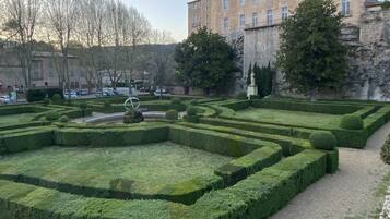 Un jardín formal con setos geométricos, una escultura central y un edificio histórico al fondo.