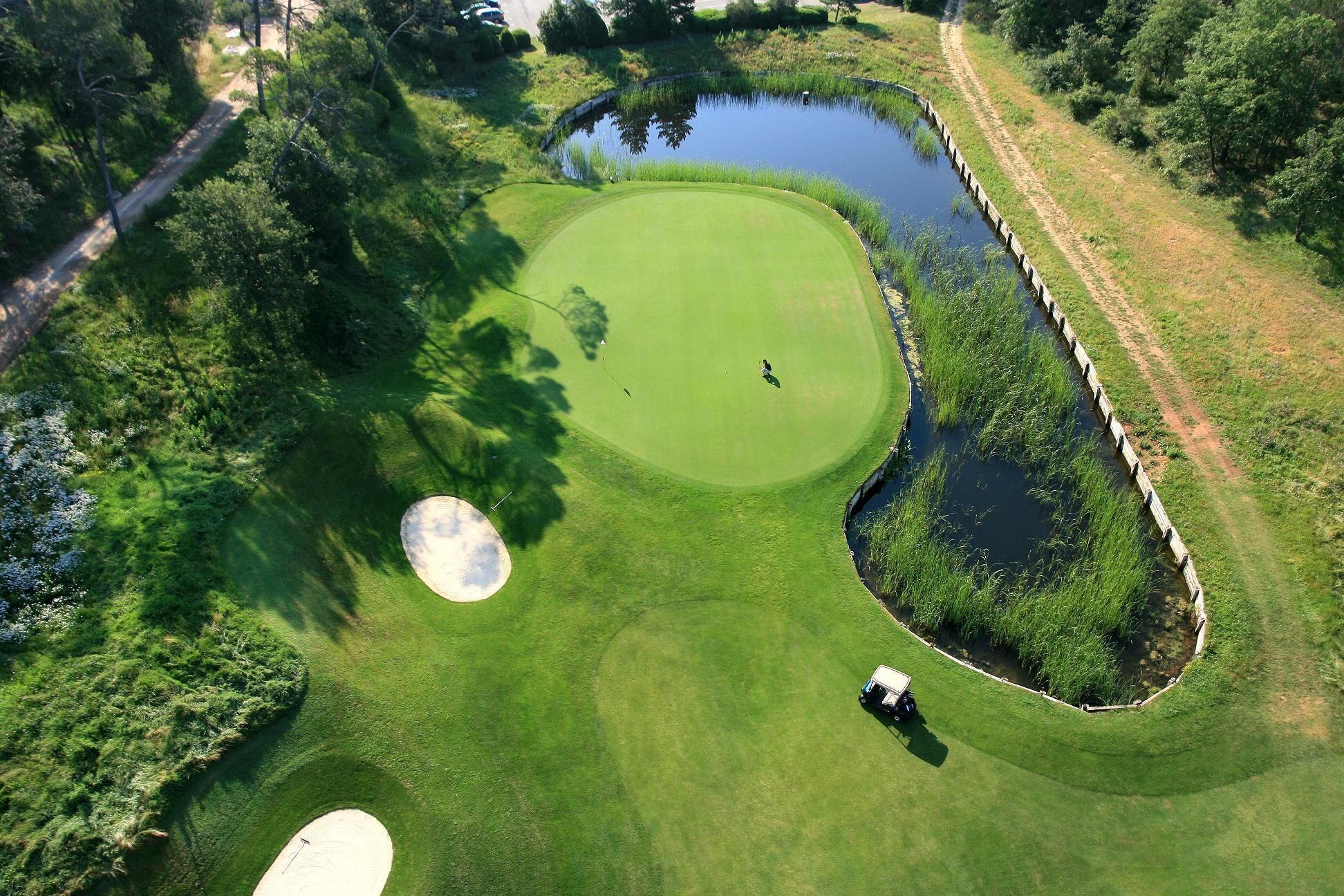 An aerial view of a golf course with a pond, sand bunkers, and a golf cart.