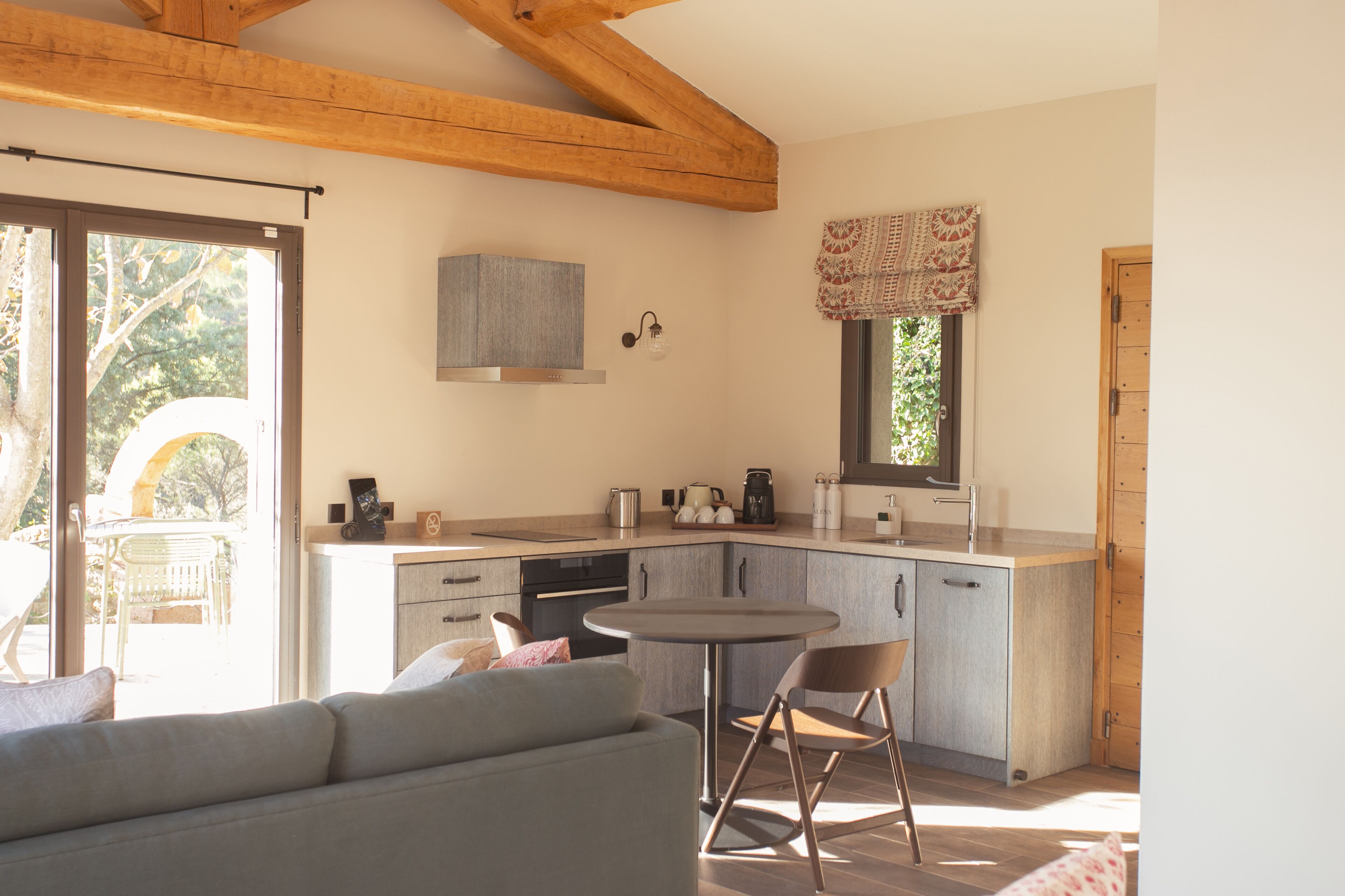 Una cocina moderna con horno empotrado, una mesa de comedor y un sofá en una habitación luminosa con vigas de madera.