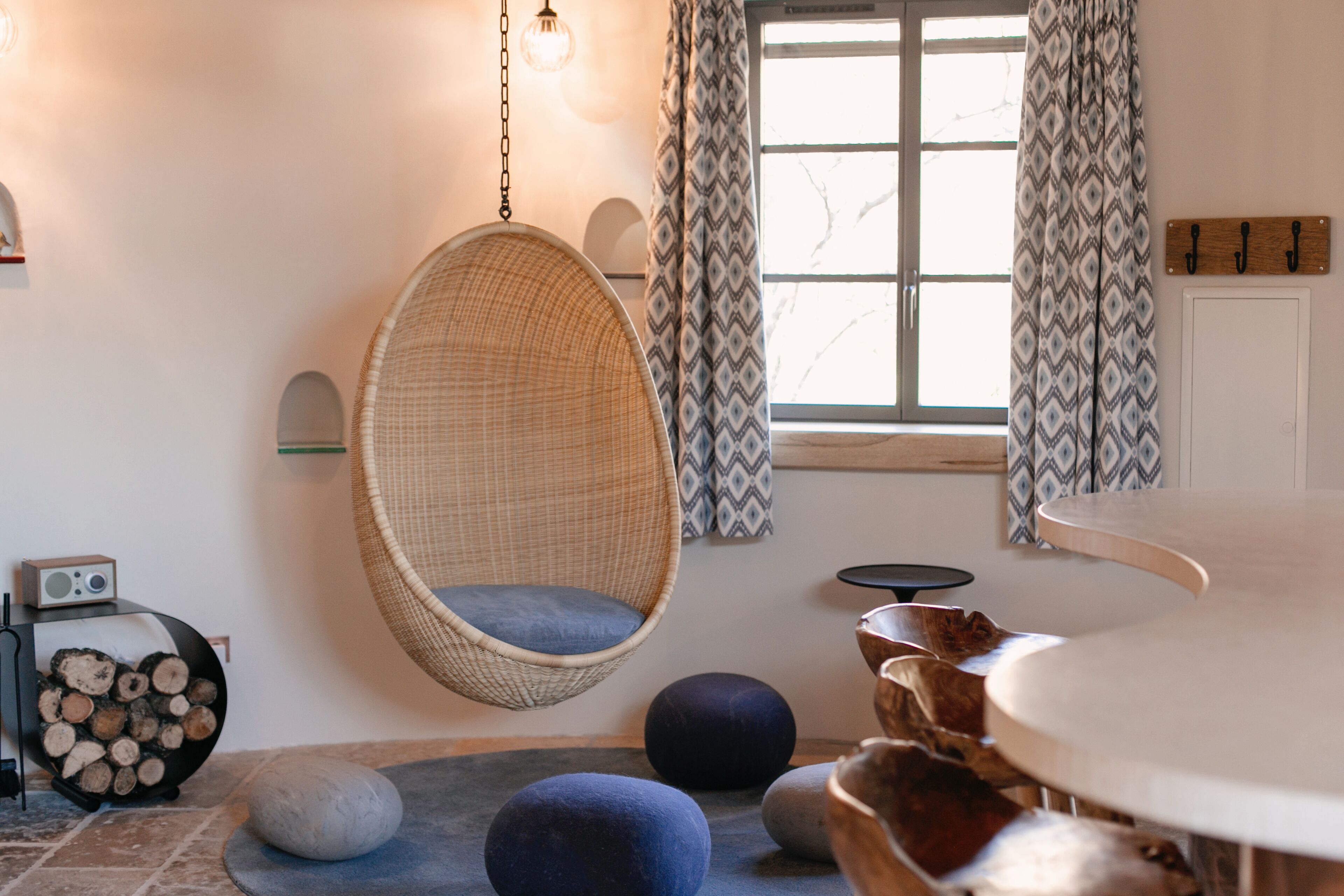 Un interior moderno con una silla colgante, mesas redondas y una chimenea con leña.