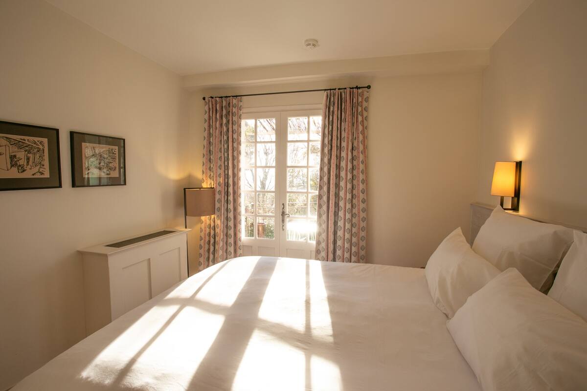 A bedroom with a bed, a radiator, a window with curtains, and wall-mounted lamps.