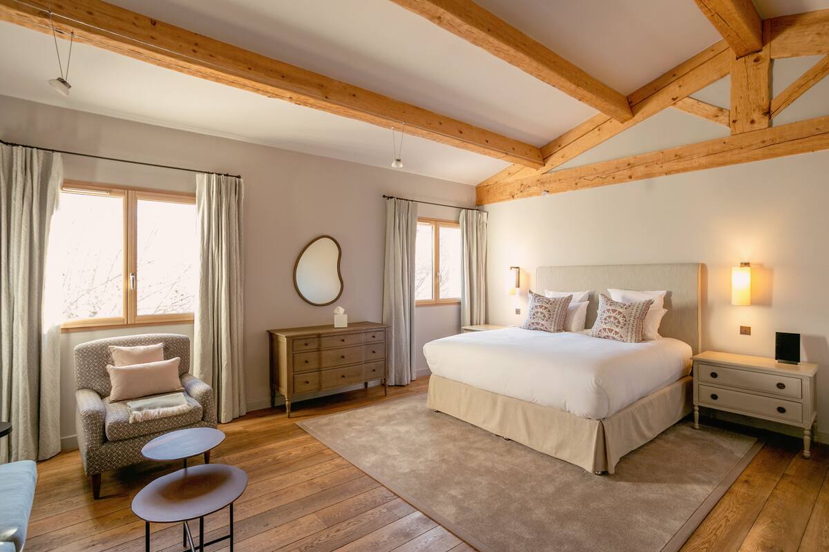 A bedroom with a large bed, a chair, a dresser, and a small table.