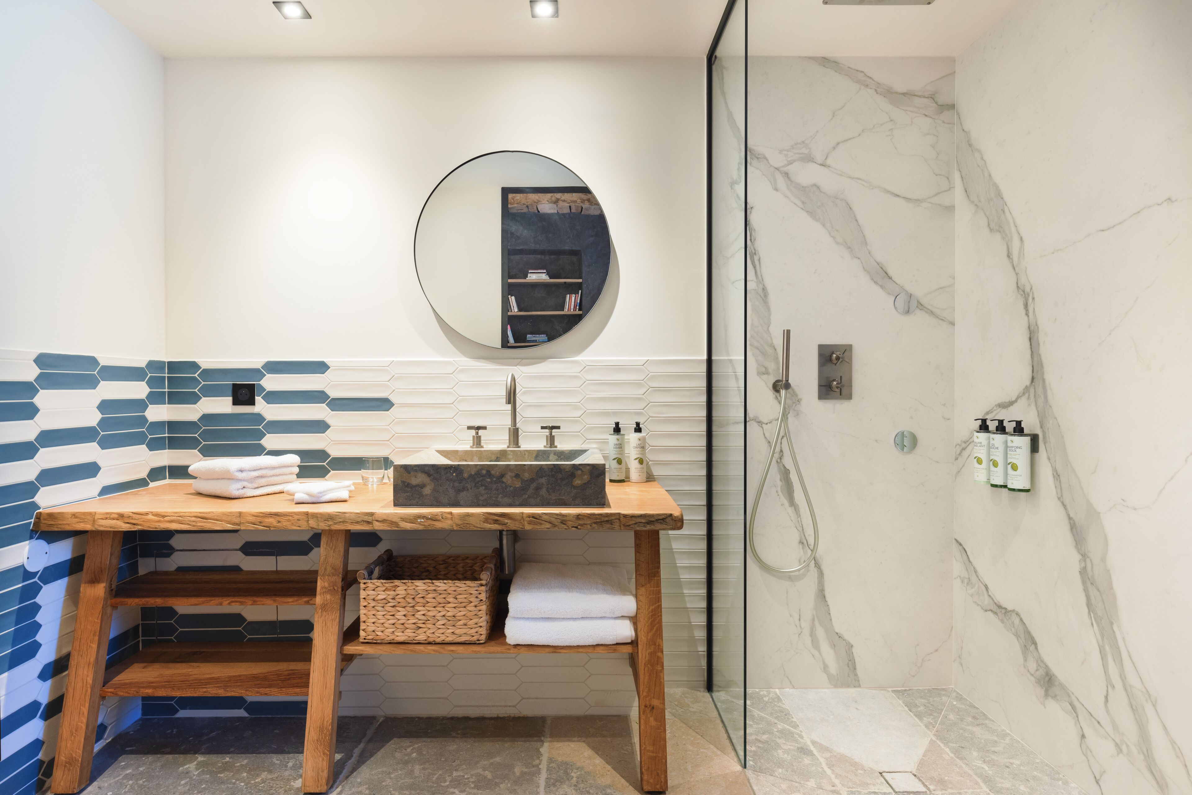 Un baño moderno con tocador de madera, un espejo redondo y una cabina de ducha de vidrio.