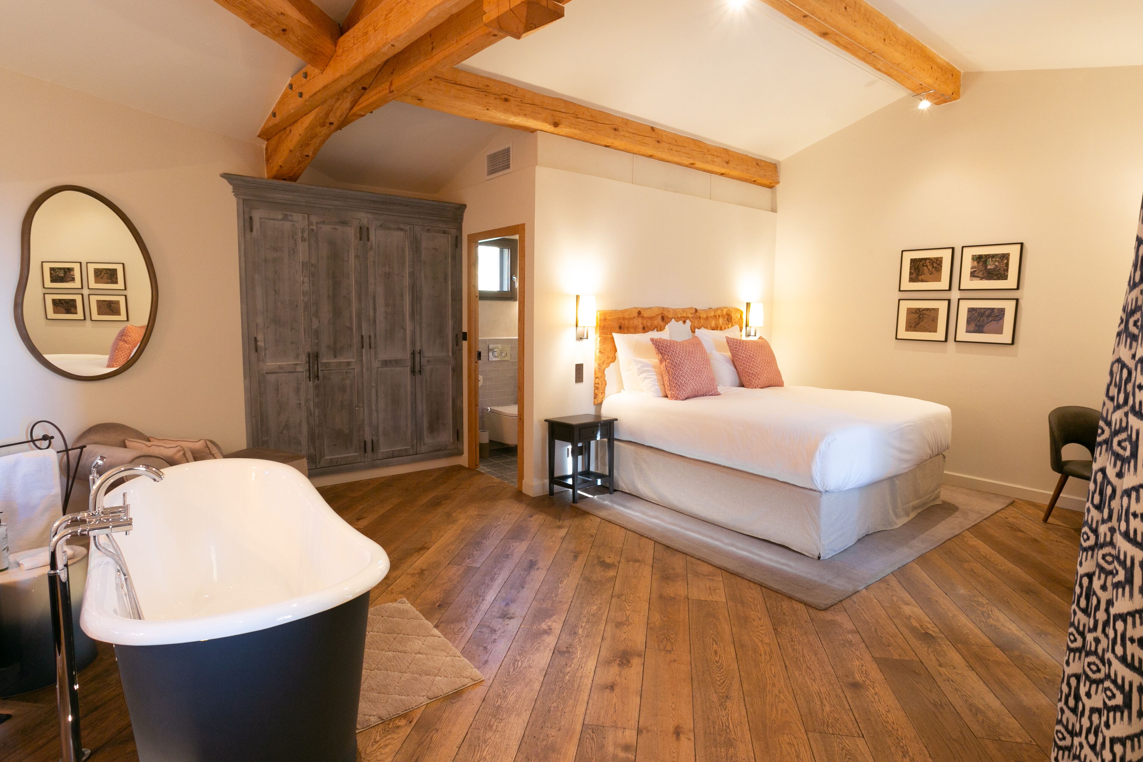 A bedroom with a large bed, a bathtub, wooden beams, and a wardrobe.