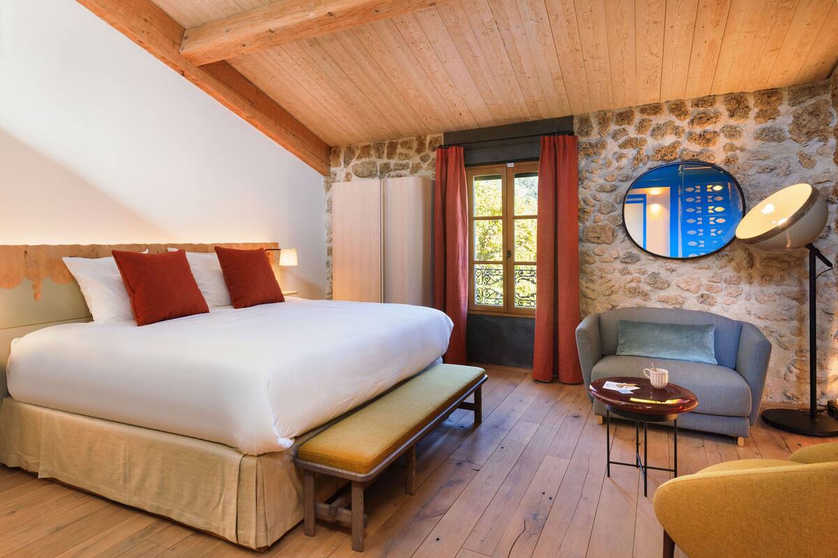 A bedroom with a large bed, a bench, a sofa, a small table, and a mirror.