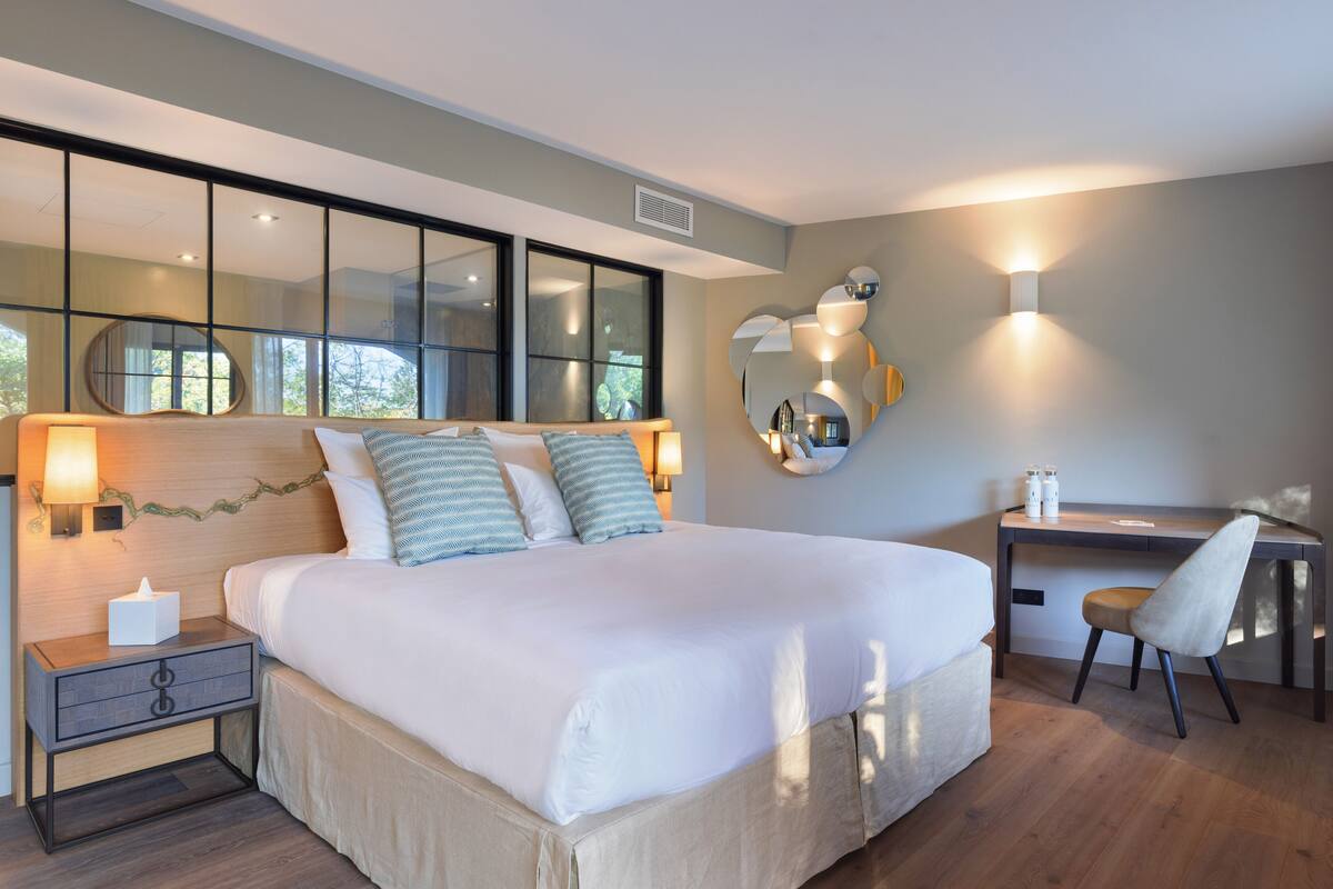 A modern hotel room with a large bed, bedside tables, a desk, and a chair.