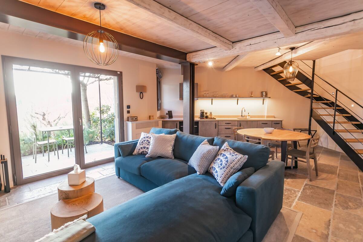 A modern living room with a blue sectional sofa, a wooden coffee table, and a staircase leading to an upper level.