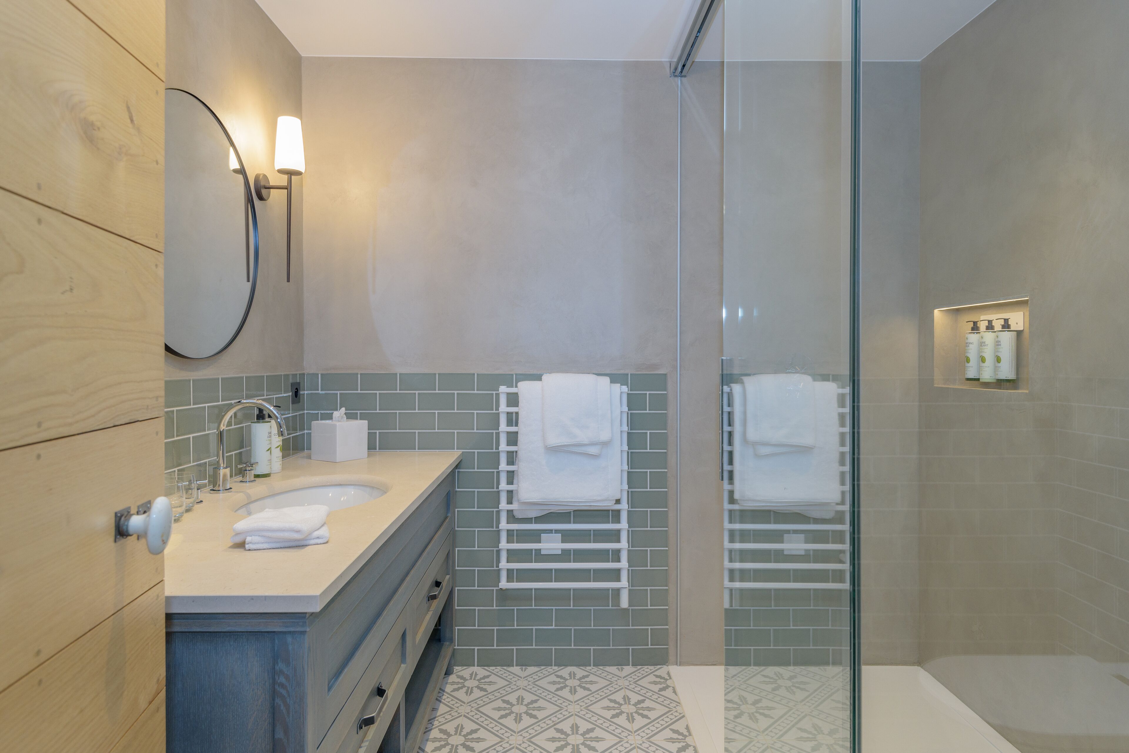 A modern bathroom with a wooden vanity, a glass shower enclosure, and a tiled floor.