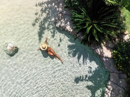 Vista aérea de una piscina cristalina con una persona flotando, rodeada de rocas y follaje.