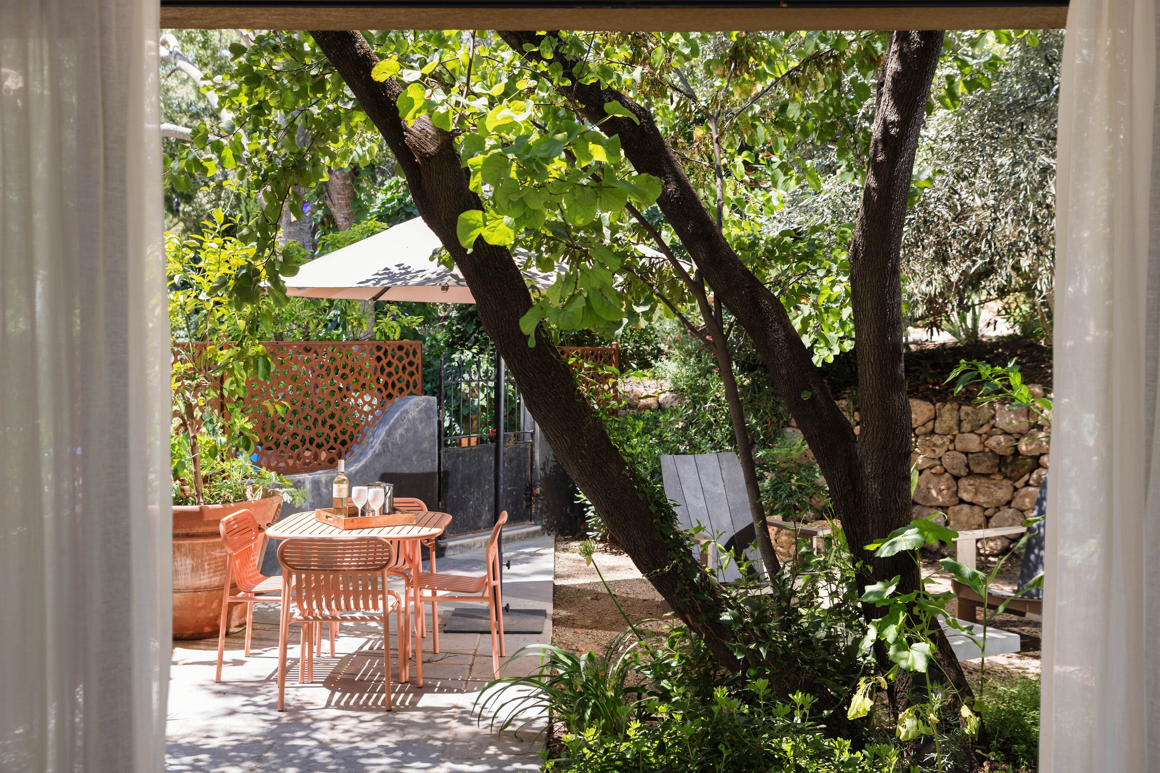Un patio al aire libre con una mesa y sillas, rodeado de follaje y un muro de piedra.