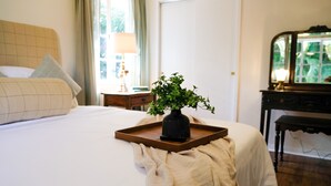 Ein ordentlich bezogenes Bett mit einem Tablett, auf dem ein Blumentopf steht, ein Nachttisch mit Lampe und ein Spiegel auf einer Kommode.