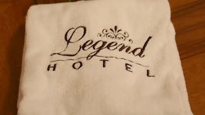 A folded white towel with "Legend Hotel" embroidered on it, placed on a wooden floor with a bouquet of flowers in the background. - Legend Hotel (Beirut)