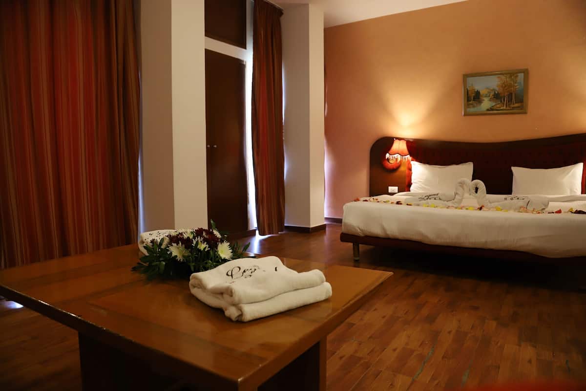 Une chambre d’hôtel avec un plancher en bois, un lit avec du linge de maison blanc, une table avec des serviettes pliées et un bouquet de fleurs.